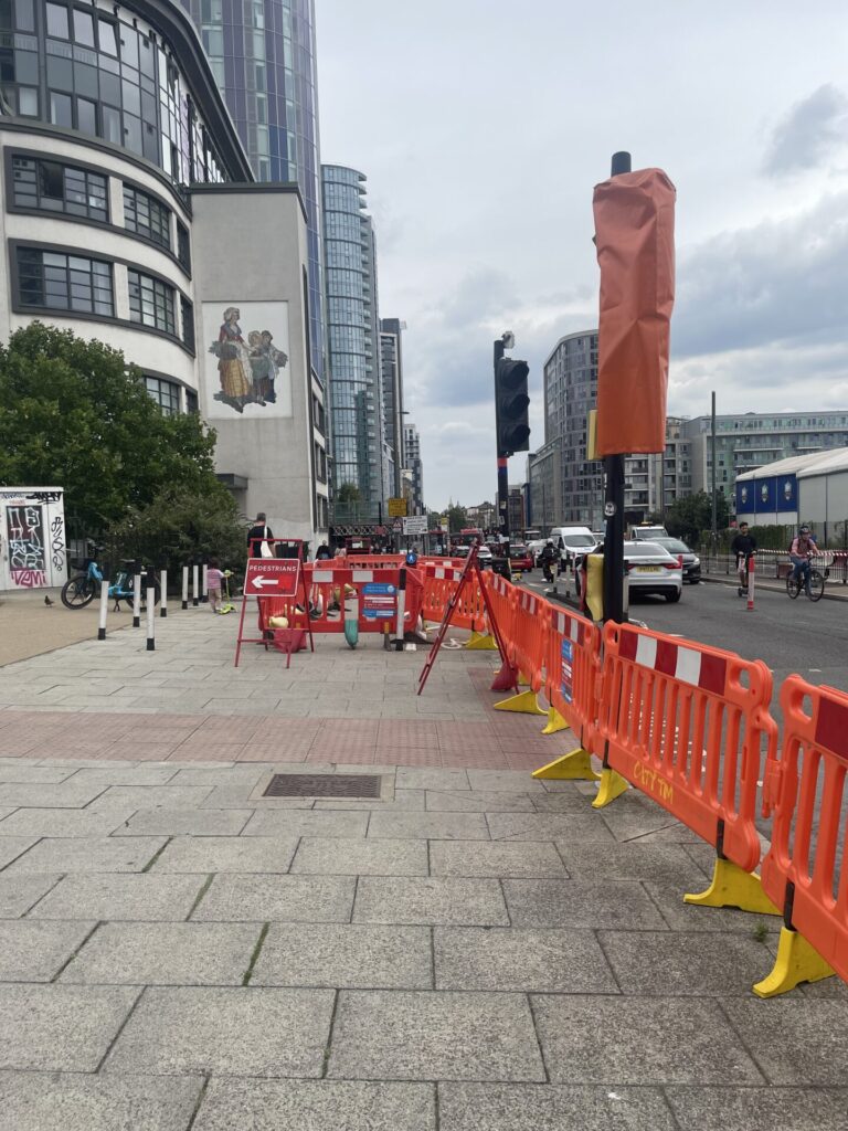 A pavement with a pedestrian crossing closed off with orange plastic fencing.