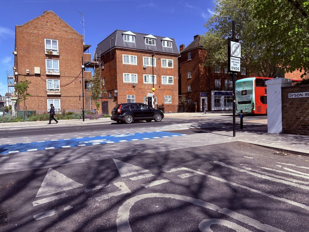 Continuous footway and cycleway over a side road of Dyson Road on a raised table, with blue surfacing on the short two-way section of cycle track.