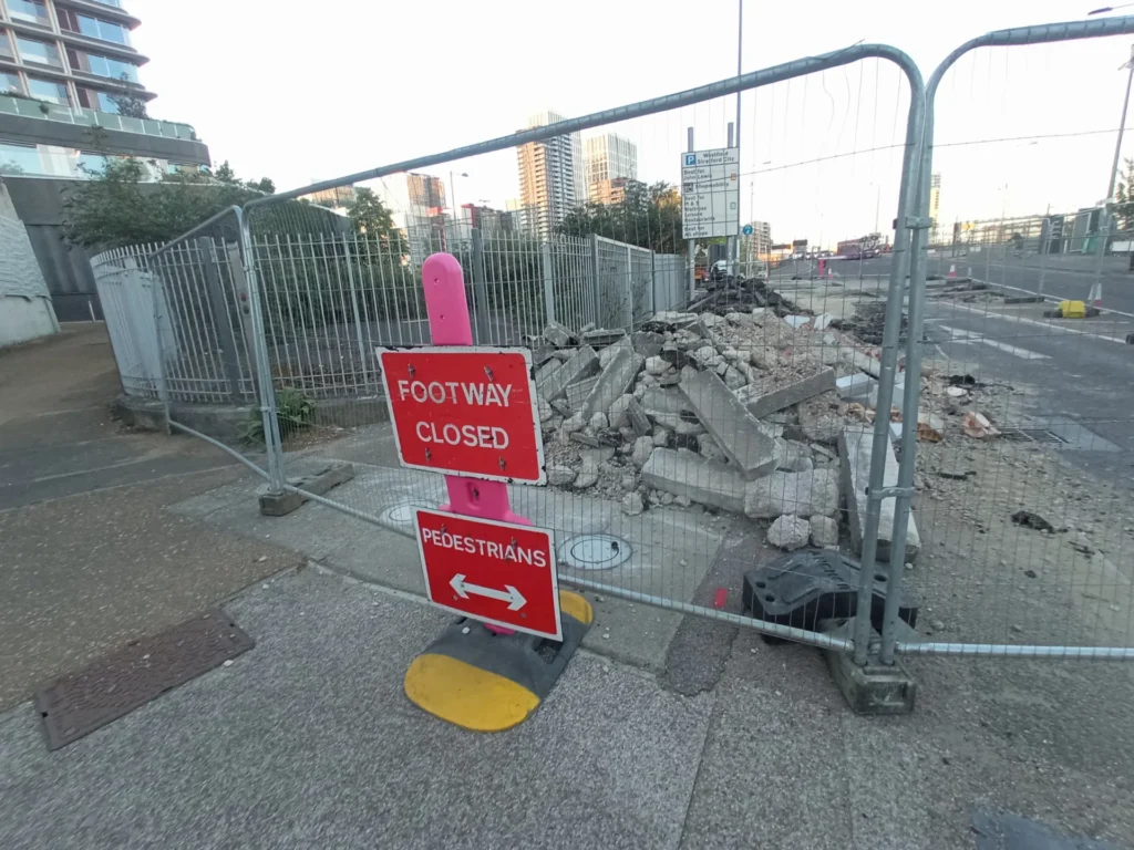 Footway closed and being excavated behind fencing.