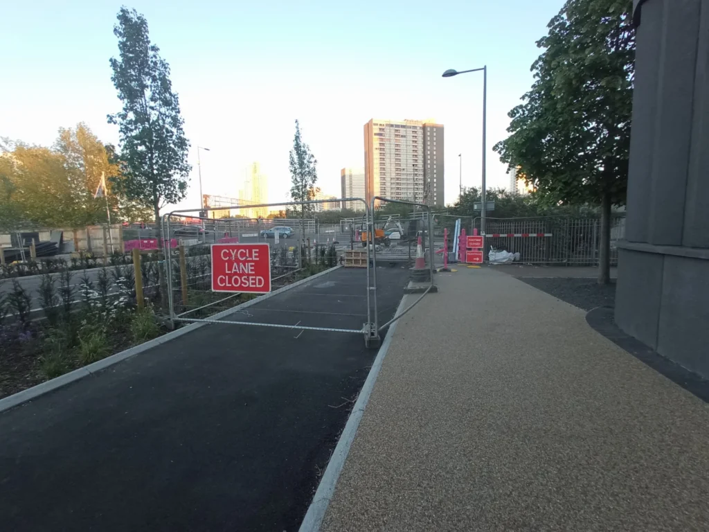 Two-way cycle track separated from road by rain garden closed with "CYCLE LANE CLOSED" fencing.